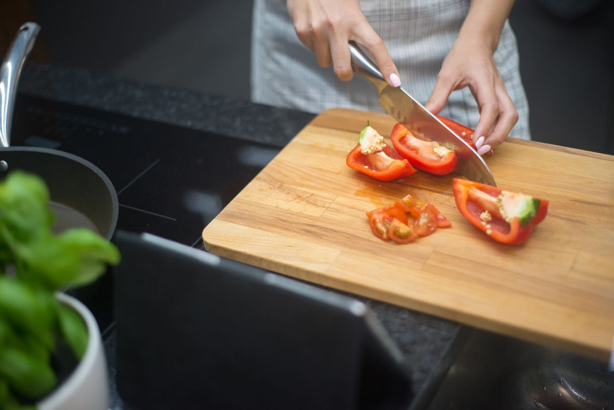 Hands slicing fresh red peppers on a wooden board in a home kitchen